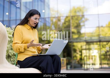Frustrated woman reacting to a laptop computer error or technical support problem, working remotely or studying outdoors with concern and stress regarding the difficult situation Stock Photo