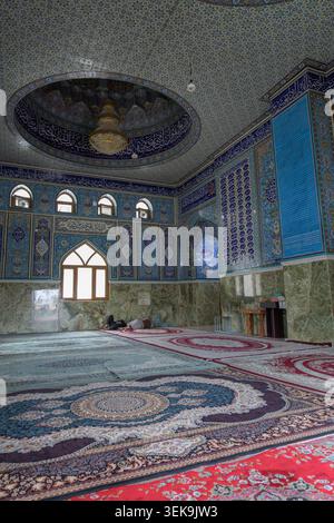 Interior of a mosque with colorful tiled walls, patterned carpets, and people praying Stock Photo