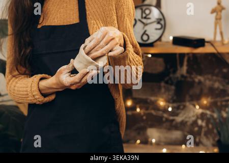 Closeup potter wearing apron holding handmade clay pot in pottery studio with blurred lights background. Creative ceramic crafting process and artisan Stock Photo