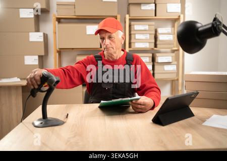 high-tech warehouse. Elderly man manager scanning parcels and checks inventory working in post office. A postman. Stock Photo