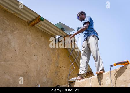 young african man installing a Starlink satellite internet antenna on the rooftop of an office in africa during installation and set up, construction Stock Photo