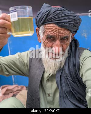 Elder man wearing a turban and traditional clothes, smiling and offering a cup of tea. Stock Photo