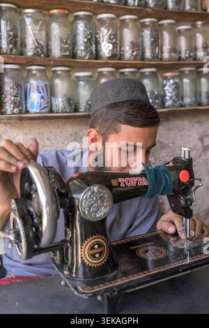 Afghan man working on a vintage sewing machine in his workshop surrounded by jars of spare parts. Stock Photo