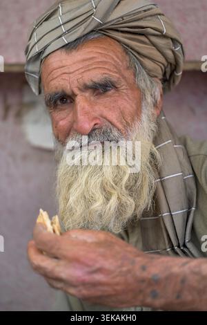 Pashtun man wearing a turban and having a long white beard, eating a piece of bread. Stock Photo