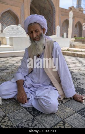Afghan man with a white turban and beard sitting on a patterned rug in Herat´s Abdullah Ansari Shrine Complex Stock Photo