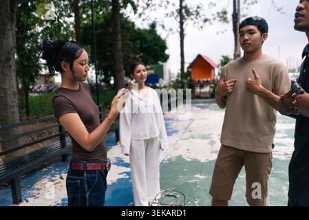 Young asian man gesturing while woman recording video outdoors Stock Photo