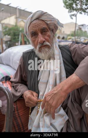 Afghan man with a white beard wearing a turban and traditional clothing, holding prayer beads in his hands. Stock Photo