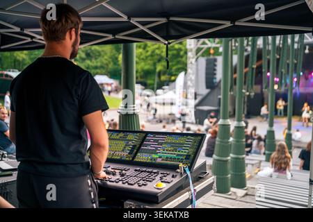 A back view shot showing a technician working behind a professional mixing desk with digital displays at an outdoor festival Stock Photo