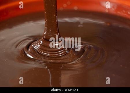 Close-up of rich liquid dark chocolate flowing in a smooth stream. Stock Photo