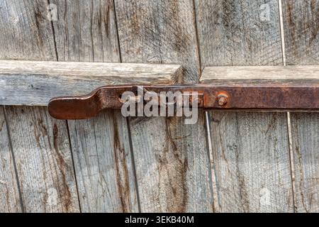 close-up shot of an old rusty metal lock mechanism mounted on a textured gray wooden plank door of a farm building Stock Photo