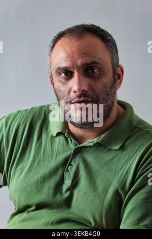 Close-up studio portrait of a serious middle-aged Middle Eastern man with a graying beard wearing a green polo shirt against a plain background. Stock Photo