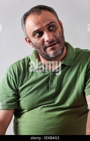 Close-up studio portrait of a Thoughtful middle-aged Middle Eastern man with a graying beard wearing a green polo shirt against a plain background. Stock Photo