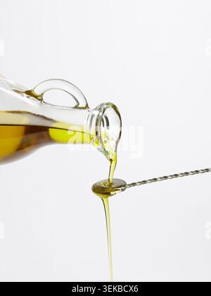 Olive oil dripping from glass bottle onto twisted cocktail spoon Stock Photo