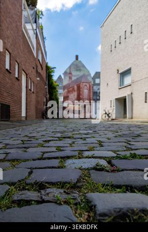 Low-angle view of narrow cobblestone alley with houses, mural and parked bicycle. Stock Photo