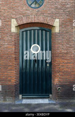 Dark green arched door with round porthole in red brick facade with stone surround. Stock Photo