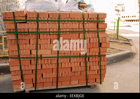 Red clay bricks stacked on pallet at construction site, building materials for house construction Stock Photo
