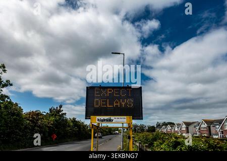 Variable message sign warning EXPECT DELAYS on a roadside in Donacarney, County Meath, Ireland, with traffic, houses, and clouds in the background. Stock Photo