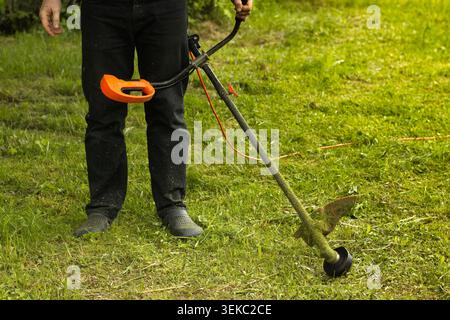 Man holding a string trimmer and cutting grass in a garden Stock Photo