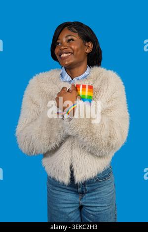 Young black woman smiling, wearing a faux fur coat and jeans, holding a rainbow mug Stock Photo