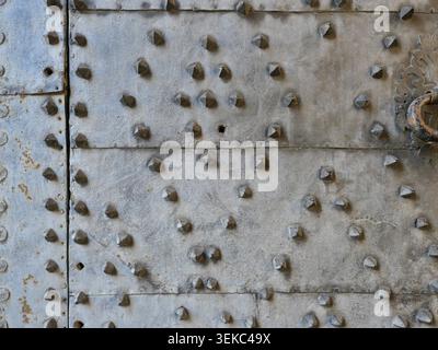 Historic metal door with riveted, textured surface and visible connecting plates. Detail view. Copyspace. Stock Photo