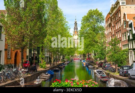 AMSTERDAM, NETHERLANDS - MAY 21, 2026: Scenic view of the historic Groenburgwal canal framed by lush green trees, featuring docked boats and the iconi Stock Photo
