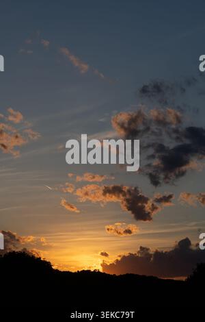 Golden sunset behind a dark hill silhouette with orange clouds, glowing evening light and a dramatic twilight landscape atmosphere. Stock Photo