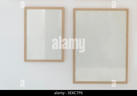 Sharp and detailed view of two empty wooden frames of different sizes hanging on a bright white wall. The minimalist mockup features blank inner space Stock Photo
