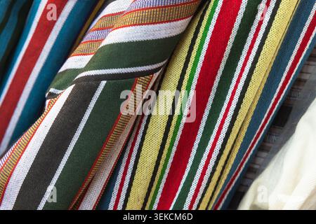 Close-up of colorful striped woven fabrics displaying vibrant traditional textile patterns and rich texture. Folded cloth features bold red, green, ye Stock Photo