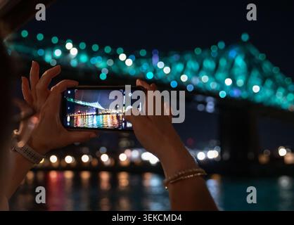 view of someone's hand taking a phone photo of an illuminated bridge at night Stock Photo