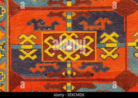 Close-up of a colorful Uzbek rug showing bold geometric motifs in orange, yellow, blue and brown tones, evoking warmth, tradition and handcrafted text Stock Photo