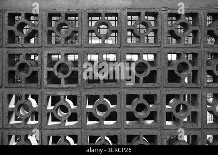 Monochrome concrete breeze block wall with repeating square and circular openings for urban architectural texture. Stock Photo
