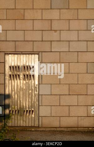 Minimal urban facade with ribbed metal door and beige block wall lit by warm sunlight and long shadows. Stock Photo