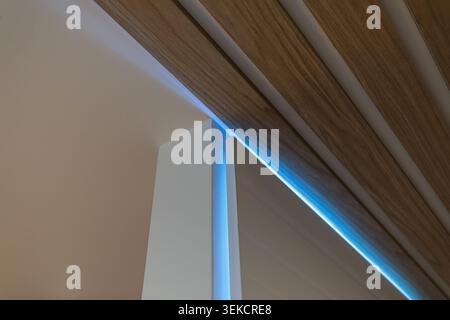 Modern architectural detail featuring wood ceiling slats, concealed blue LED accent lighting, clean geometric lines Stock Photo