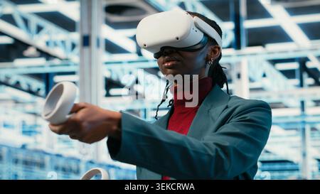 Data center smiling programmer uses VR headset technology to visualize equipment powering internet services. Happy server farm expert uses virtual reality simulation to oversee systems, camera B Stock Photo