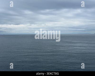 Calm ocean water texture beneath layered gray clouds, creating a minimalist seascape background with subtle ripples and natural blue tones. Stock Photo