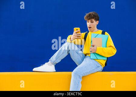 Surprised college student reading news on smartphone on colorful background Stock Photo