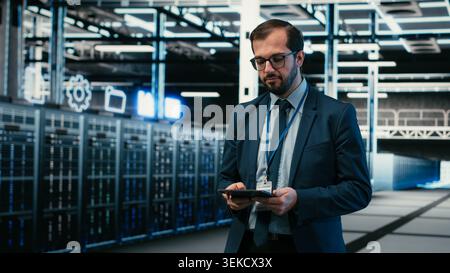 Data center software developer using tablet and augmented reality to install upgraded server racks systems. Employee using automation app on device to monitor server hub, VFX overlay, camera B Stock Photo