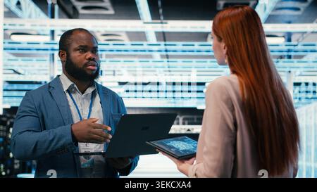 Data center team of technicians uses AI deep learning on devices to optimize performance. Software developers brainstorm how to integrate neural network automation in data center operations, camera B Stock Photo