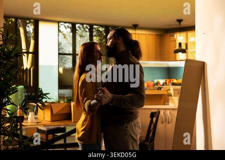 Young partners hugging and dancing among cardboard boxes in their new house indoors. Romantic moment capturing the happiness and satisfaction of homeowners celebrating fresh start. Stock Photo