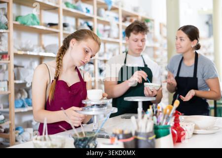 Pottery master together with his students applies a pattern to pottery in workshop Stock Photo