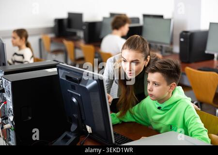 Female teacher consulting tween boy studying in computer class Stock Photo