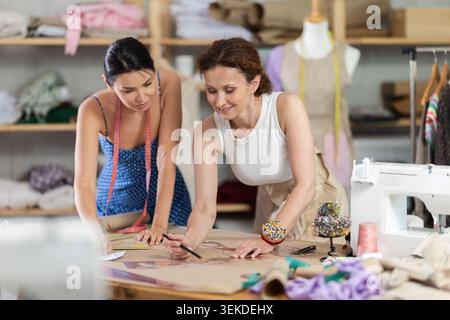 Two female tailors draws pattern on a sheet of paper in sewing workshop Stock Photo