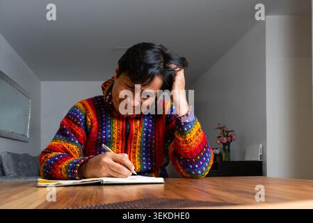Man feeling frustrated while trying to write in his notebook at home Stock Photo