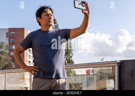 Mature man taking a selfie outdoors on a building rooftop against a blue sky Stock Photo