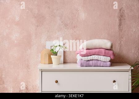 Stack of knitted sweaters on white dresser in room Stock Photo