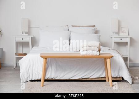 Stack of knitted sweaters on bedside bench in bedroom Stock Photo