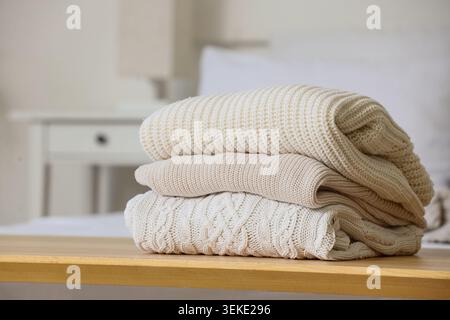 Stack of knitted sweaters on bedside bench in bedroom, closeup Stock Photo