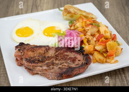 Breakfast steak and fried eggs complete with potatoes and garnished with onion. Stock Photo
