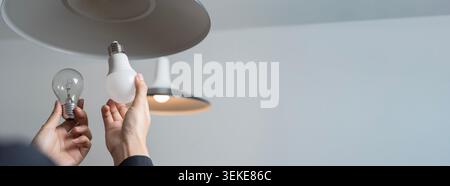 Hands replacing an old bulb with modern LED light under a ceiling lamp, showing energy saving, home maintenance, electricity efficiency and sustainabl Stock Photo