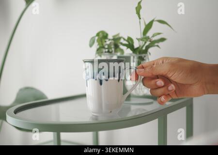 Hand holding cup on green tray with plants nearby Stock Photo